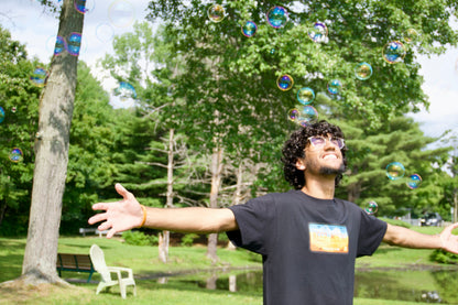 Black tee being worn while running through bubbles, smiling. 