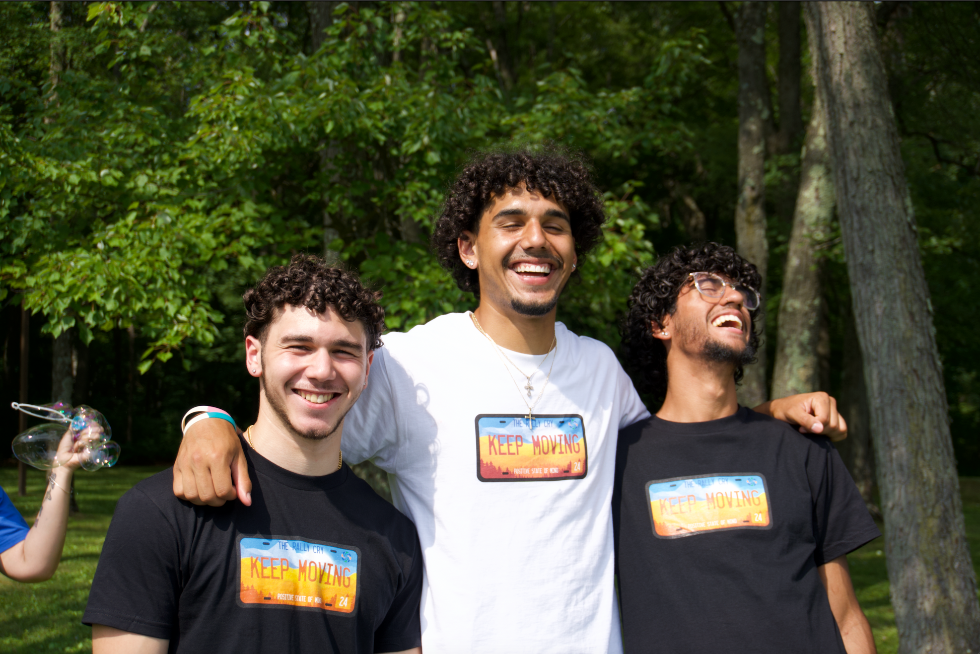 3 men wearing keep moving tees with one wearing white and others wearing black, laughing together. 
